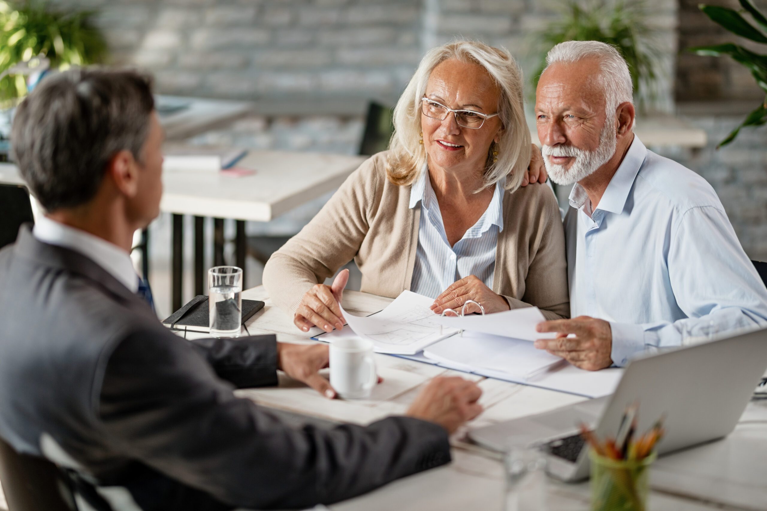 Happy mature couple talking with real estate agent while analzying housing plans on a meeting in the office.
